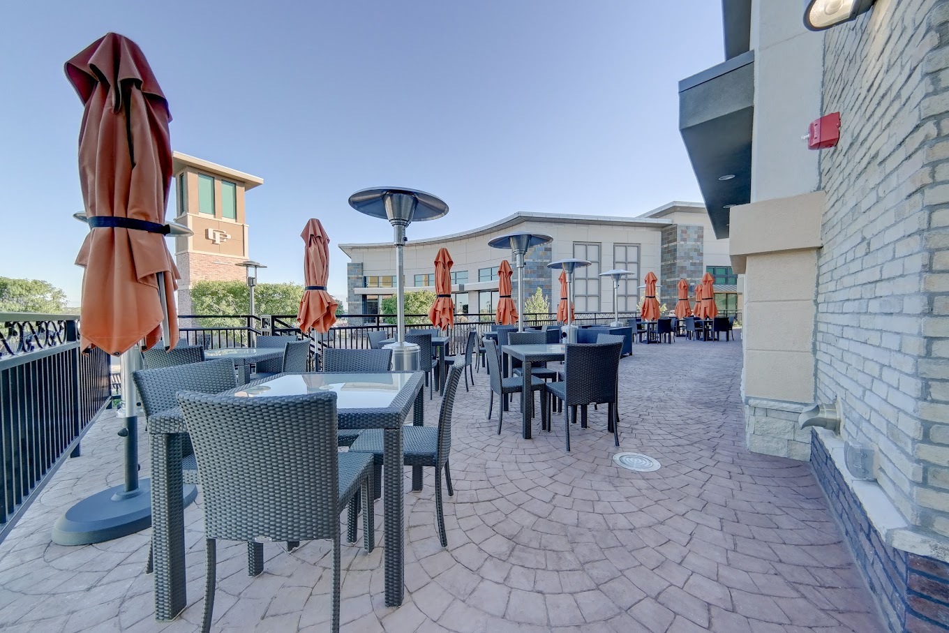 An landscape view of a restaurant patio, full of tables and chairs- the tables have orange umbrellas.