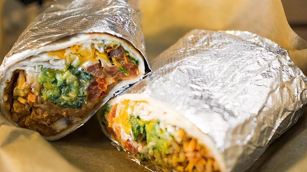 A burrito on a plate, cut in half and wrapped in tin foil.