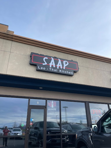 An outside view of a restaurant, with a black sign and a large windows out front.