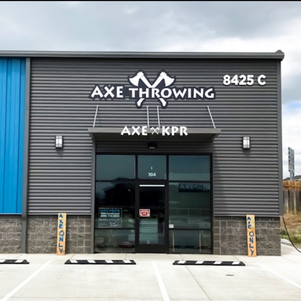 An outdoor view of a modern style building with a blue accenting on the walls, a white sign reading "Axe Throwing"