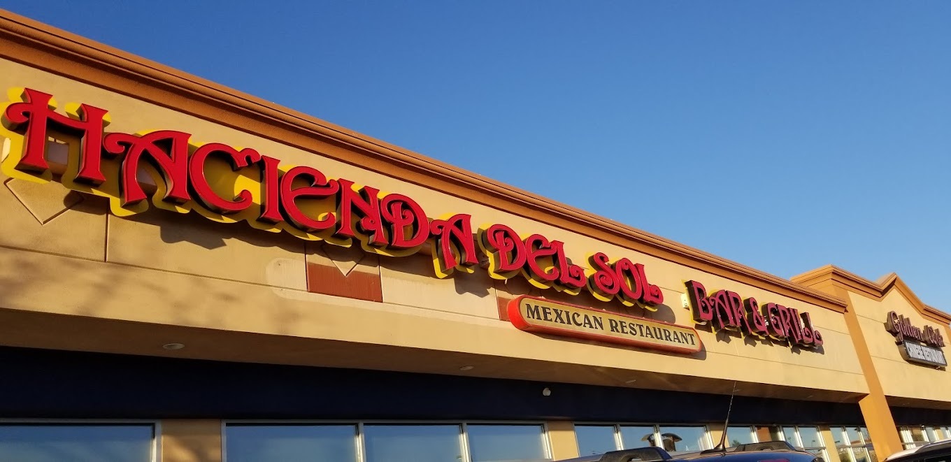 An outside view of a restaurant with red lettering out front "Hacienda Del Sol"