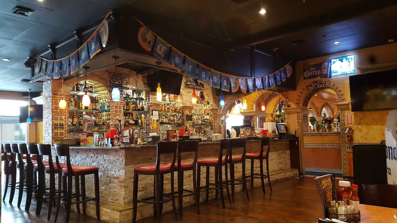 A view of a bar in the wall made of bricks, lined with chairs and a decorative banner hangs above the bar.