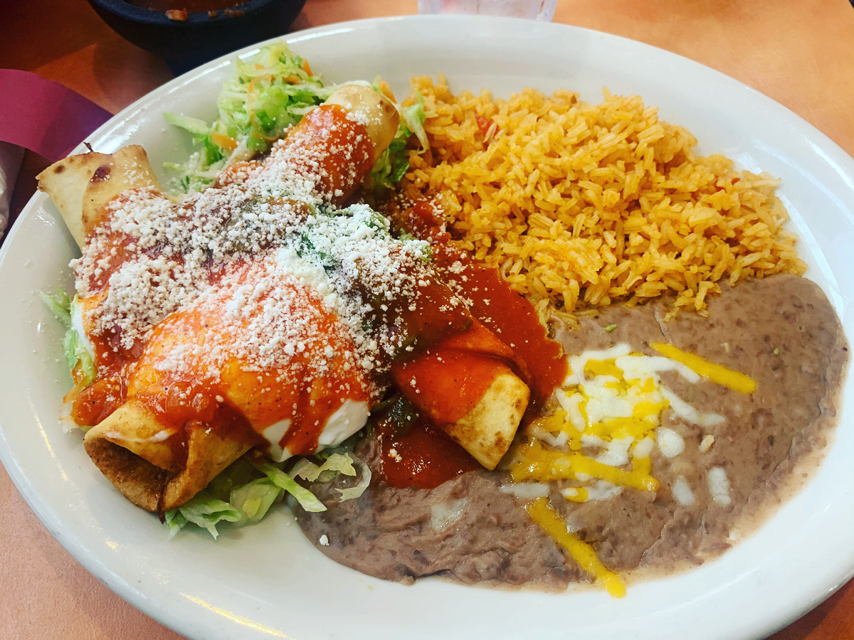 A white plate with three tacos, a side of refined beans, with rice.