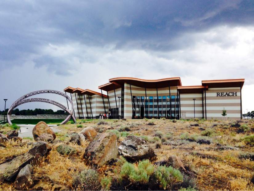 A large striped modern style building, with a large circular statue out front and surrounded by desert.