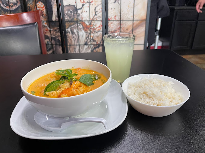 A white serving plate with soup garnished with large green leaves and a side of white rice in a white bowl.
