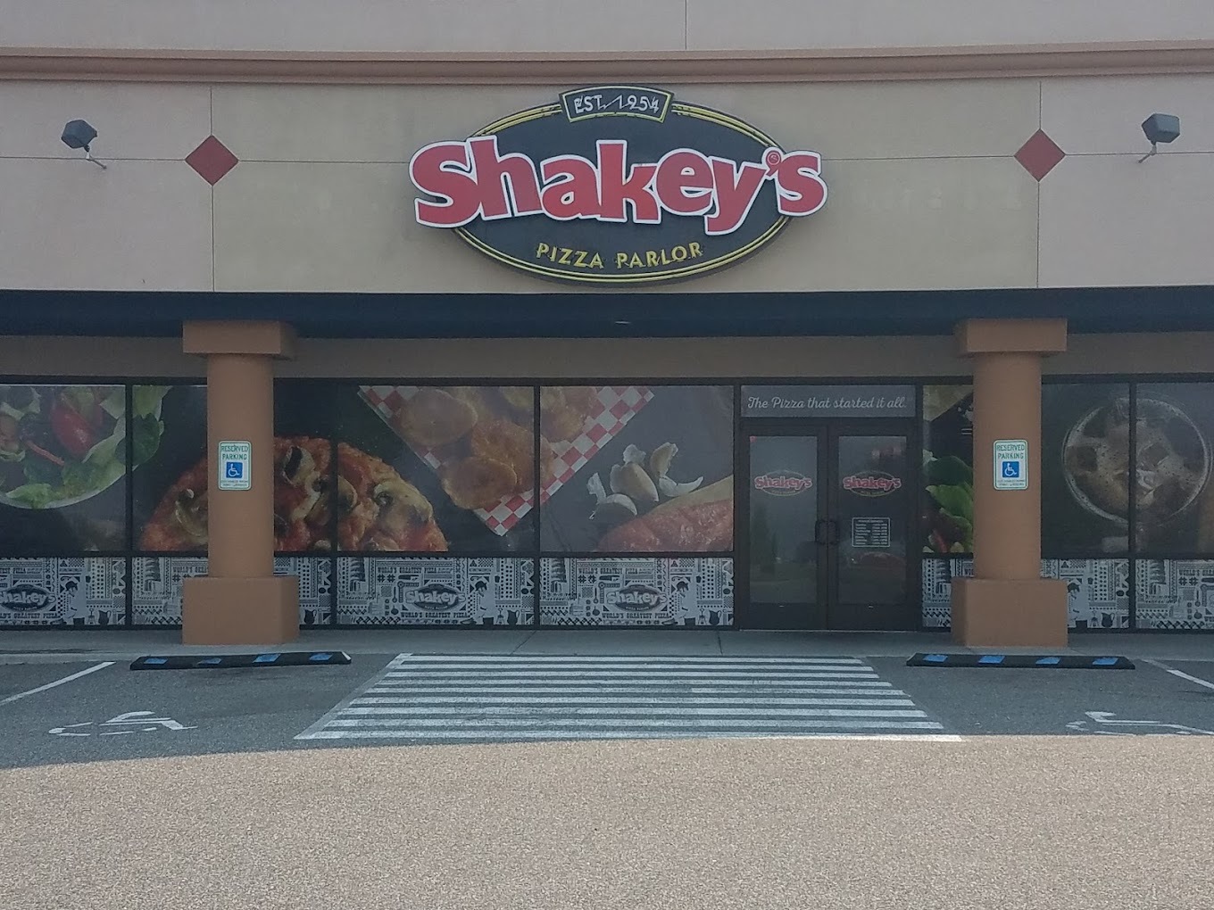 An outside view of a restaurant with a red and black sign out front, two brick podiums set out front.