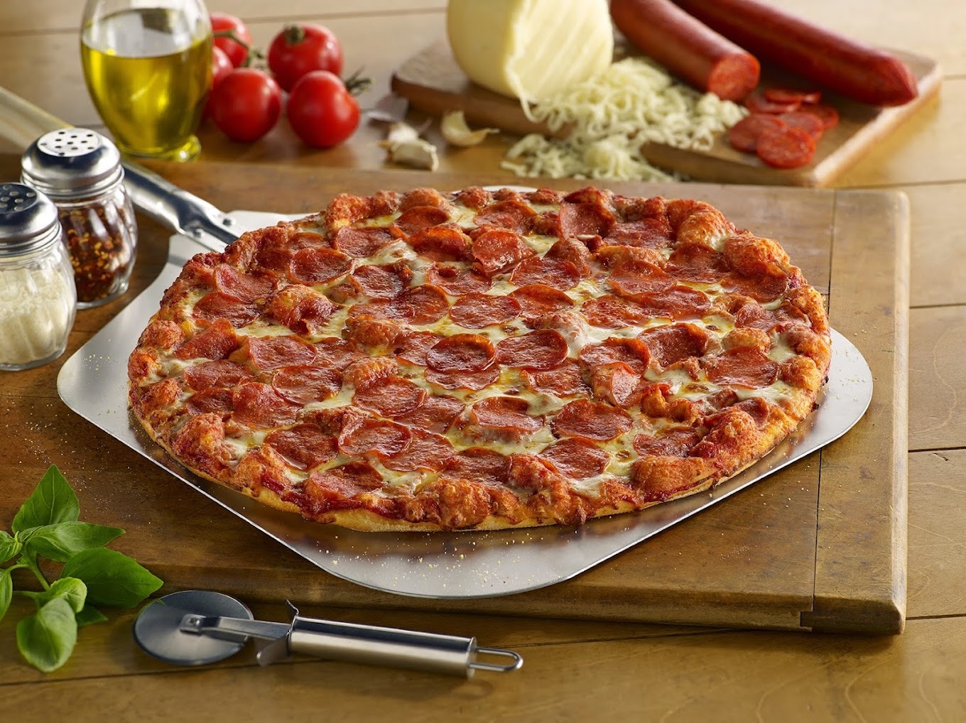 A large pepperoni pizza staged with all the ingredients laid out on the side of the pizza, along with a pizza cutter.