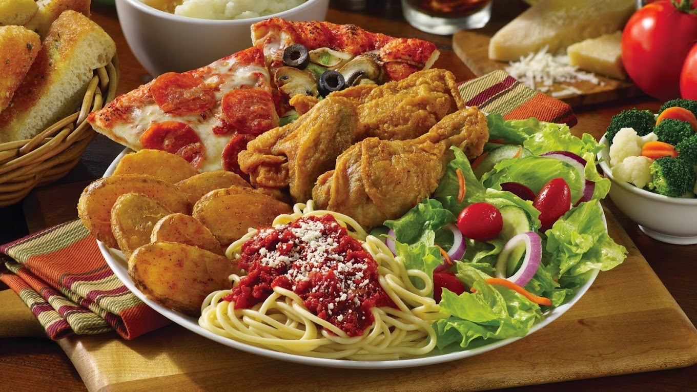 A silver food platter with all kinds of foods from spaghetti, chicken wings, a side salad, pepperoni pizza.