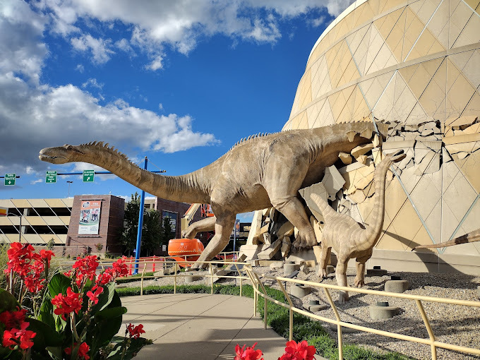 Exterior view of the museum, which has two statues of dinosaurs, made to look like they are walking out of the building.