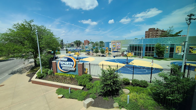 Exterior outside view of the Sports Legends Experience play area. There is a black fence and green shrubbery.