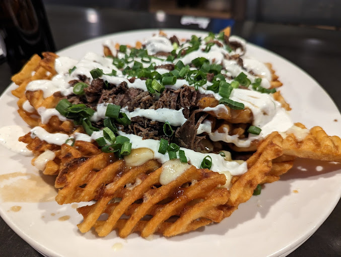 Meat, greens, and sauce over cross-hatch fries on a white plate.