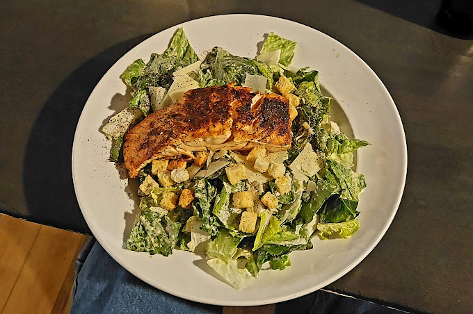 Chicken salad with greens on a white plate in a dim room.