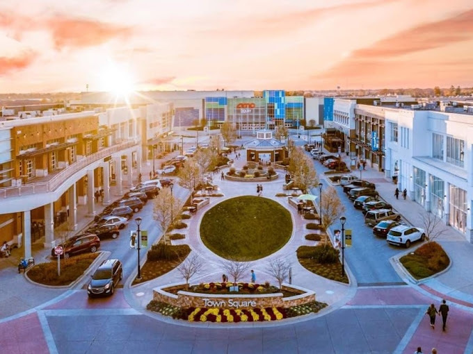 Exterior aerial view of a shopping center with a central green area during sunset.