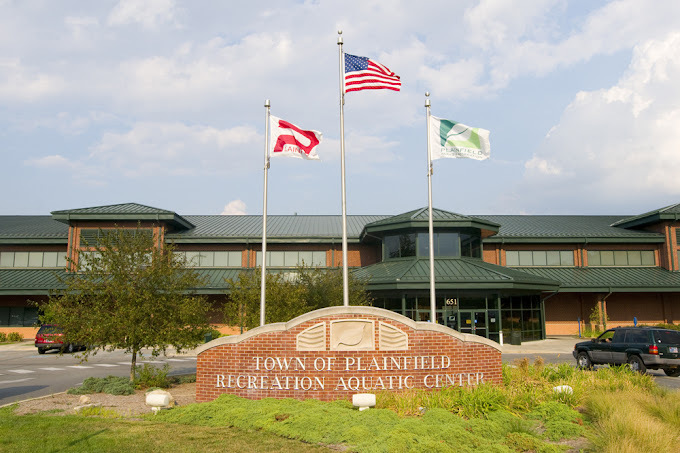 Exterior view of a green and red brick building. A brick based sign is in front of the building, with three flags coming from the center of the sign.