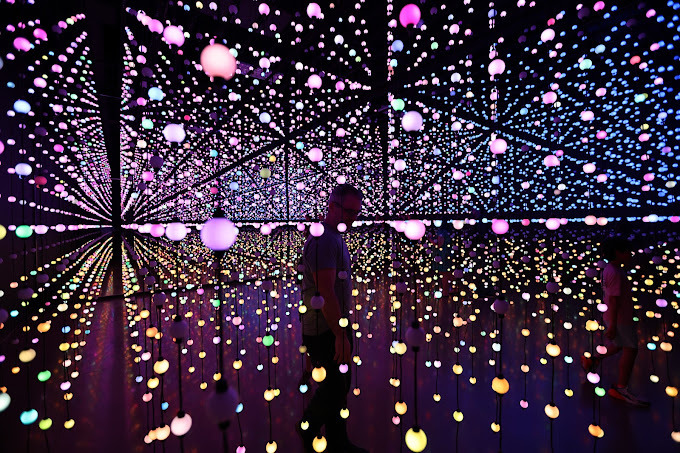 Dark, colorful room of glowing circles hanging from the ceiling. It is mainly pink, purple, yellow, and some blue.
