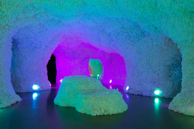 Cave-like room with textured walls and a purple, green, and blue glow.