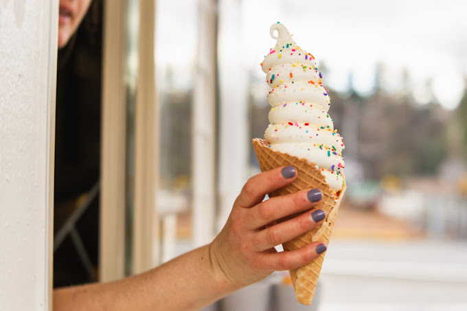 Woman holding an ice cream cone containing vanilla ice cream and sprinkles outside a drive-thru window.