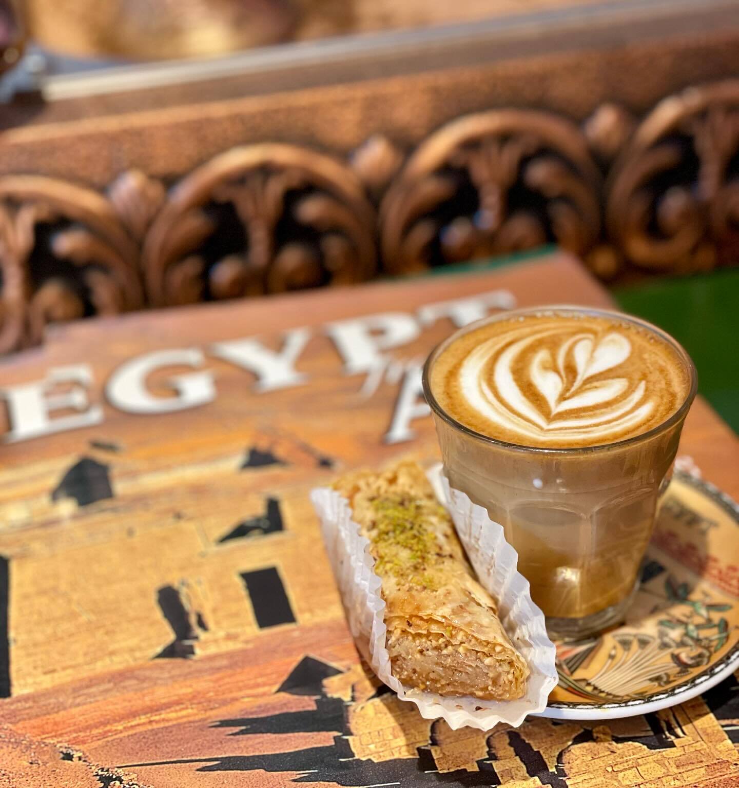 Latte with heart latte art and a baked good on a table that has images of Egypt, as well as Egypt written out in white lettering.