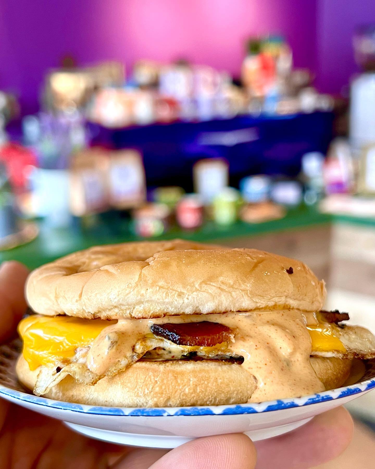 Burger with egg, sauce, and cheese on a blue plate. A hand holds the plate, with the background being the food creation corner.