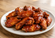 Plate of glossy barbecue chicken wings coated in rich sauce on a wooden table with warm natural lighting.