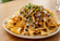 Plate of loaded nachos topped with melted cheese, shredded meat, black beans, jalapeños, and fresh cilantro on a wooden table with a softly blurred background.