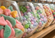 Close-up of glass candy bins filled with colorful assorted candies in pastel shades on a wooden shelf with a softly blurred background.