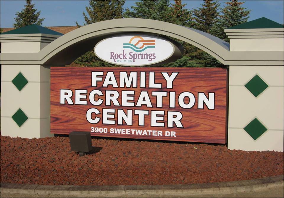 A view of a concrete sign setting out front of a rec center that is beige and red with white lettering.