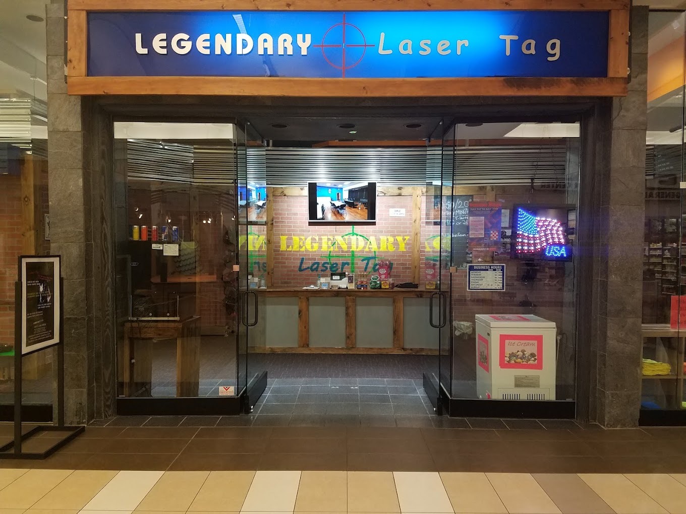 A view of the mall entrance to a laser tag place inside of a mall a large blue sign with white lettering reading "Legendary Laser Tag"