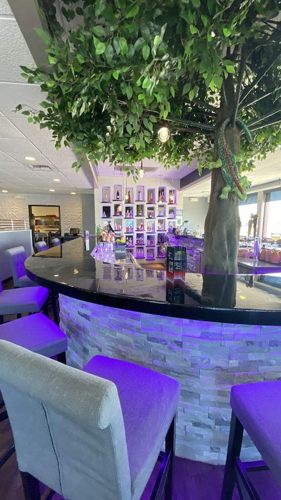 A view of a modern styled bar with led lights underneath the bar and a fake tree in the bar.
