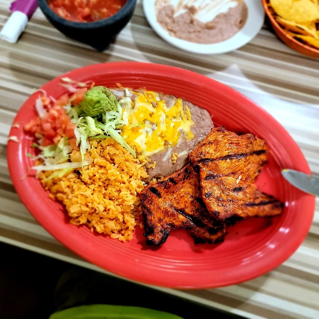 A red plate consisting of a side of rice and beans alongside steak main course.