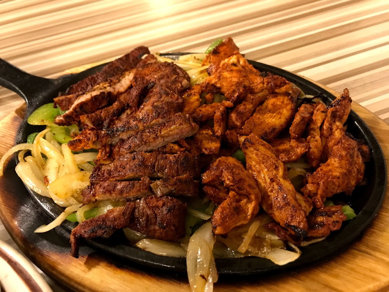 A wooden serving tray with a skillet consisting of onion, greens, and topped with grilled chicken.