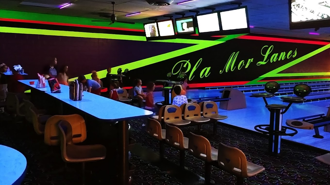 A view of a bowling alley with a neon painting on the wall that reads Pla Mor Lanes illuminated by black light.