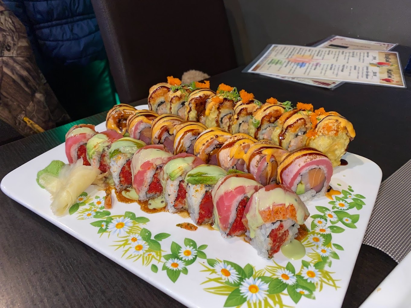 A large white serving plate consisting of three long rows of different kinds of sushi, the plate is decorated with white flowers.