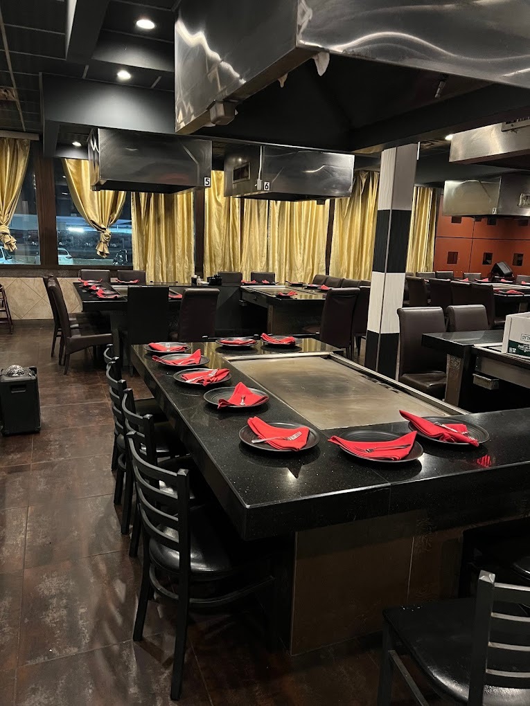 A view of a dining room with hibachi grills and ventilation hoods over the grills, chairs surround the grill counter for patrons to watch them cook and eat their food right there.