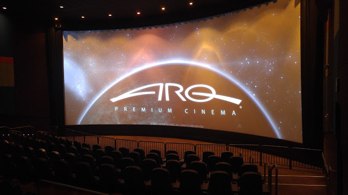 A view of a very large theatre screen, which looks curved from so far away, a dark room with many rows of seats.