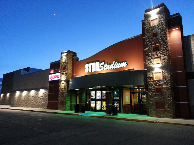 A outside view of a theatre entrance at dusk, lights illuminate the pillars of the entrance along with an illuminated sign reading "Star Stadium"