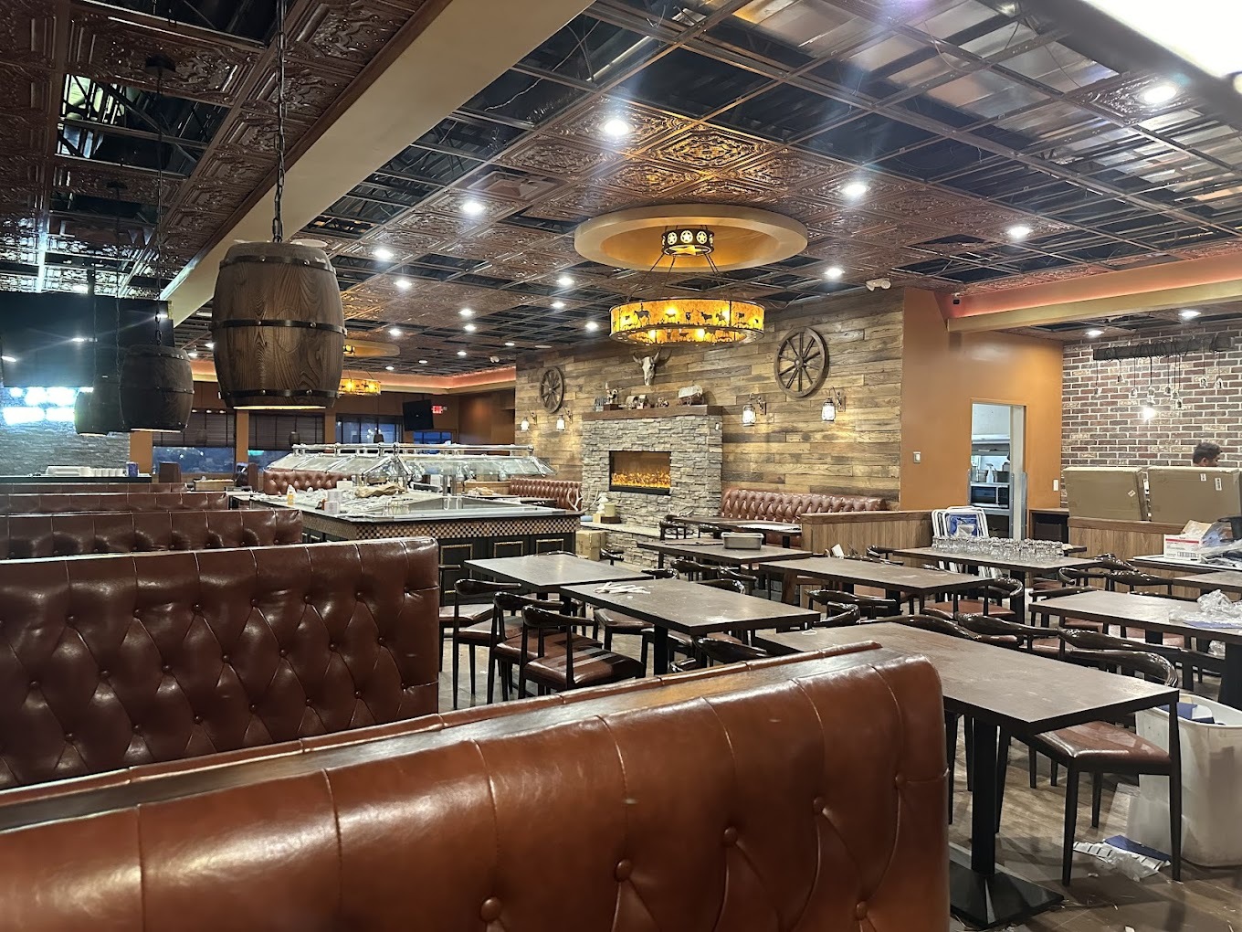 A view of a restaurant dining area from a booth, intricate designs on the ceiling and a large chandelier, a buffet is in the back center of the dining room.