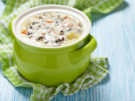 A green mug consisting of soup on a blue table with green fabric underneath the green soup bowl with handles.