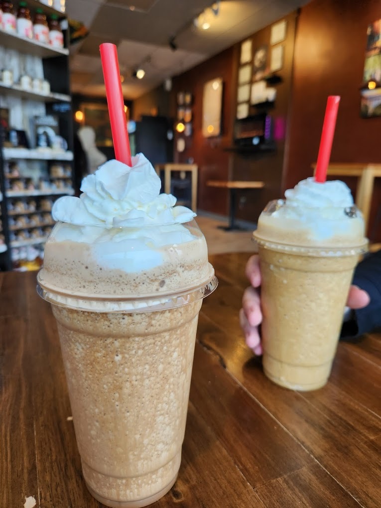 A table with a view of two blended drinks topped with whipped cream and red straws.