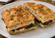 Toasted focaccia-style sandwich layered with sliced turkey, melted cheese, fresh spinach, tomato, and a creamy herb spread on a white plate.