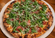 Wood-fired style pizza topped with pepperoni, fresh arugula, grated Parmesan, and melted cheese on a rustic ceramic plate over a wooden table.