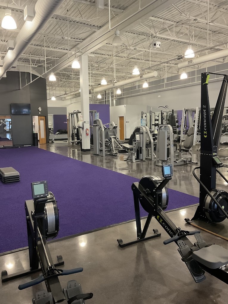 A large room with a large purple carpet on the floor, in a room full of workout equipment such as bikes, weights, and cardio equipment.