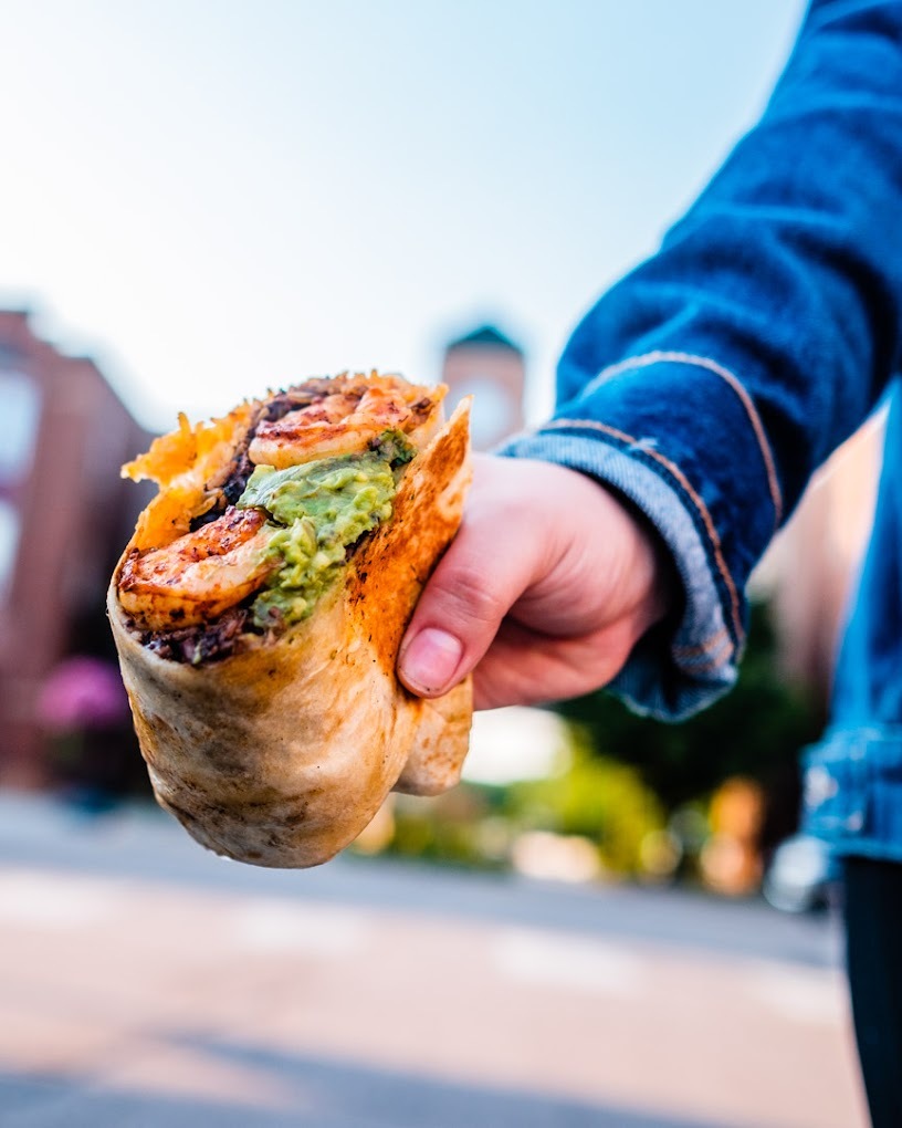 A view of a person holding a burrito consisting of meet, guacamole and cheese.