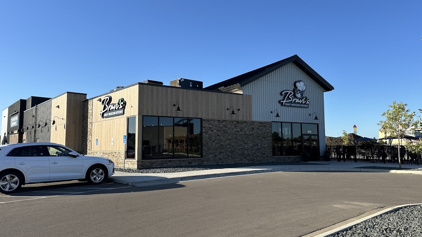 An outdoor view of a restaurant with wooden paneling and metal siding along with a sign with white lettering reading "Bravi's"