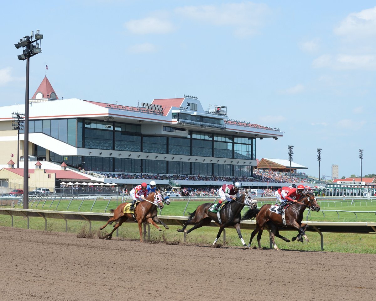A view of a horse racing track with three men on horses racing down the track.