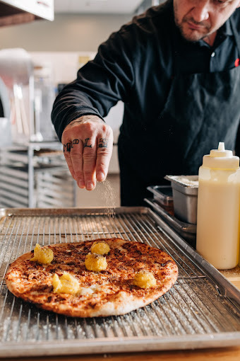 A view of a chef sprinkling cheese onto a pizza on a prep pan.