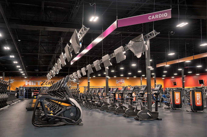 Rows of grey fitness equipment with orange accenting and orange walls.