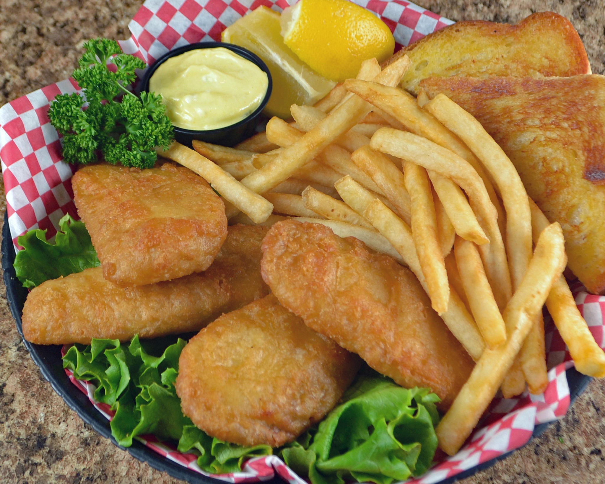 Breaded chicken, fries, toast, lettuce, and dippable sauce, all set in a red and white checkered paper inside a basket.