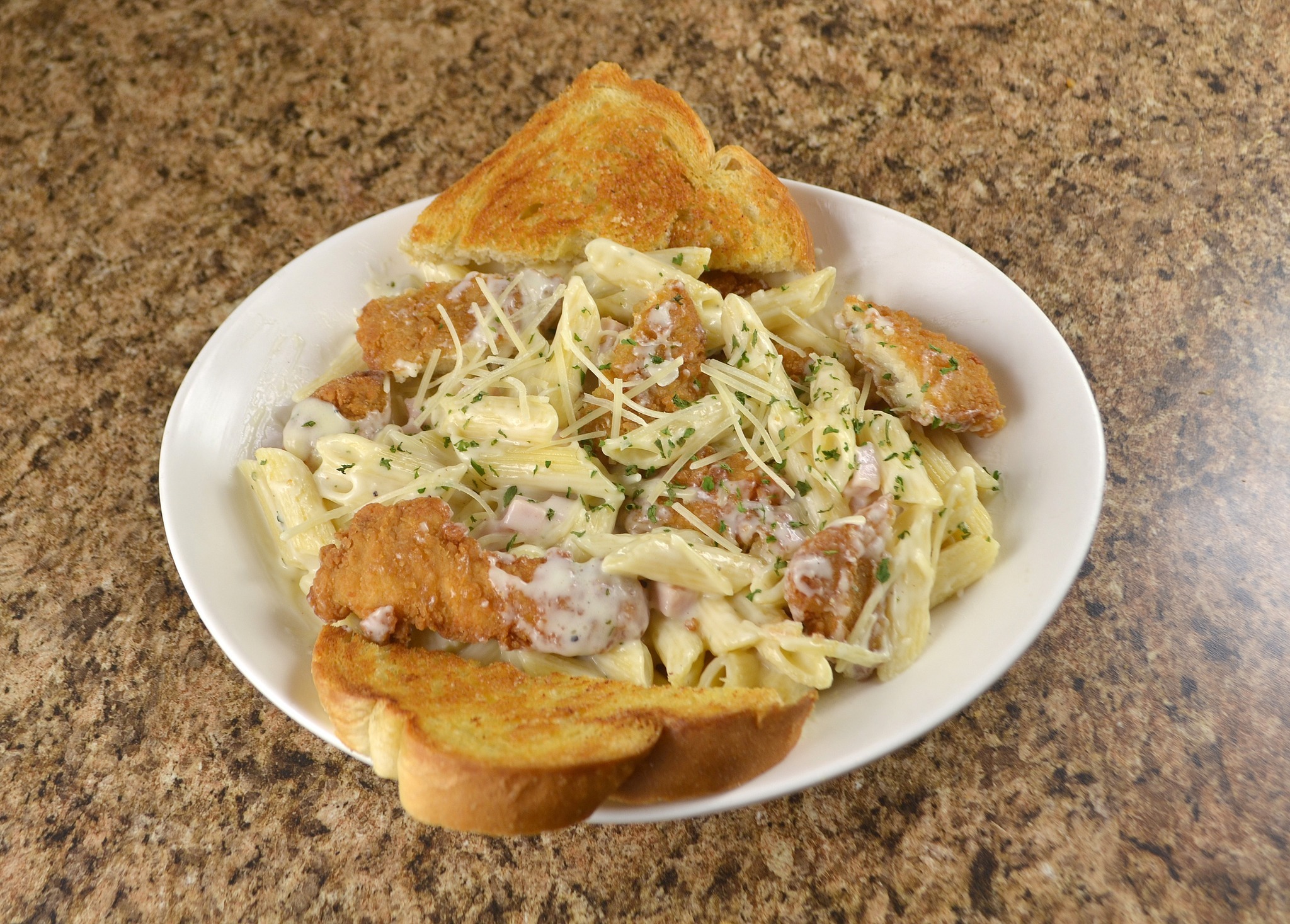 Close view of past, chicken, and bread on a white circular plate, on top of a granite counter.
