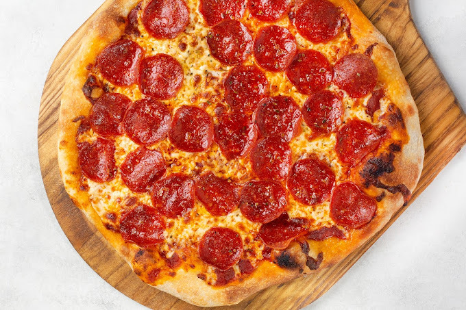 A view of a pepperoni pizza on a wooden pizza board.